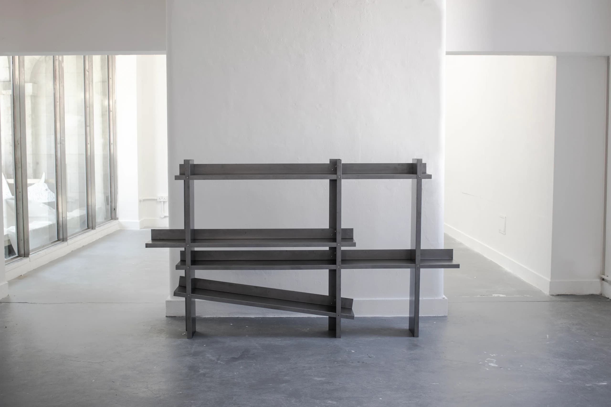 A low, wide folded-steel shelf against a white studio wall, above a polished concrete floor.